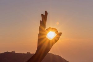 A hand frames the sun at sunset over the Thoptewadi hills, India.