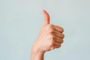 Close-up of a hand showing a thumbs up gesture on a blue background.